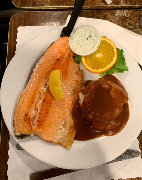 A plate with grilled salmon, a lemon wedge, a slice of orange, lettuce, and mashed potatoes with brown gravy.