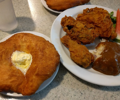 A plate with fried chicken, mashed potatoes with gravy, and a fried dough pastry with butter on the side.