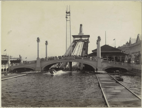 Historic photo of a bridge with a slide, people gathered, and a waterway, capturing a vintage amusement park scene.