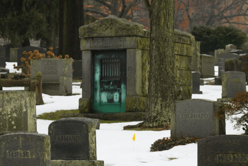 A mysterious, weathered mausoleum with a glowing green door, surrounded by snow-covered gravestones in a cemetery.
