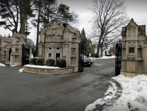 Gated entrance with ornate stone architecture, surrounded by snow and trees on a cloudy day.