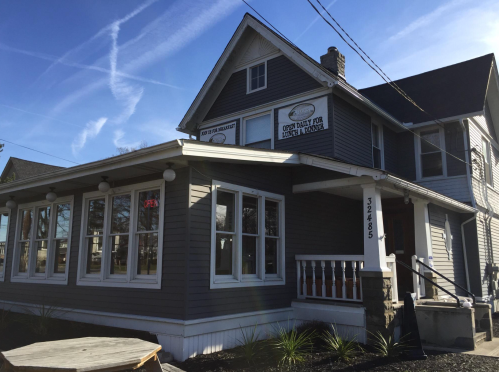 A gray two-story house with a sign that says "Open Daily for Lunch & Dinner" and an "Open" neon sign in the window.