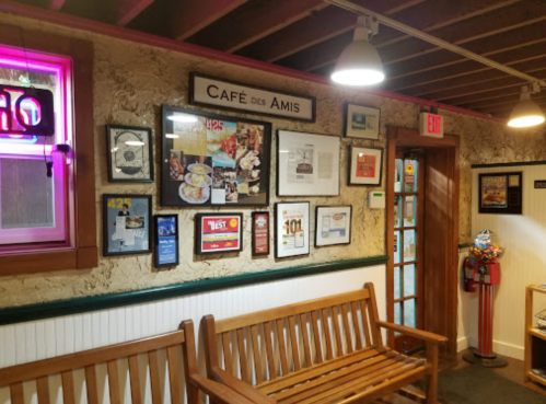 Interior of Café des Amis featuring a wooden bench and a wall adorned with framed photos and awards.