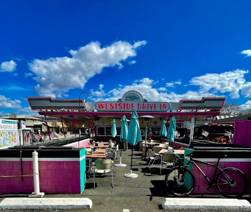 A colorful drive-in restaurant with outdoor seating and umbrellas under a bright blue sky with clouds.