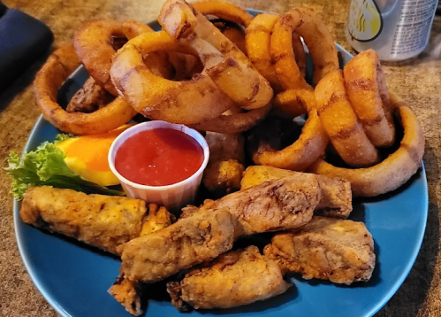 A blue plate filled with crispy onion rings, fried chicken strips, and a small cup of dipping sauce.
