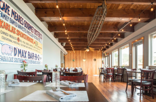 Interior of a restaurant with wooden beams, tables set for dining, and a large mural on the wall. Warm, inviting atmosphere.