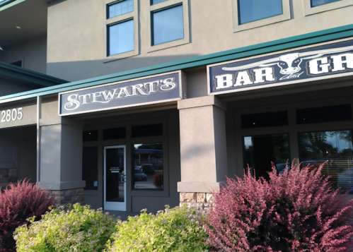 Exterior view of a building featuring signs for "Stewart's" and "Bar & Grill," with decorative plants in front.