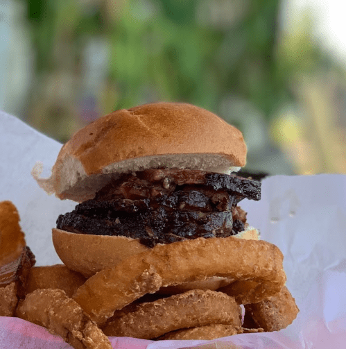A close-up of a juicy burger on a bun, served with crispy onion rings on the side.