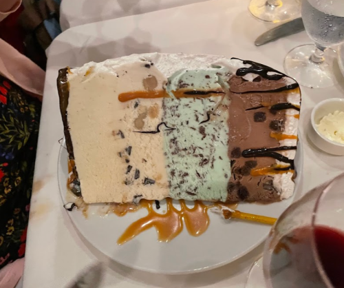 A large slice of layered ice cream cake with chocolate, mint, and vanilla flavors, drizzled with caramel sauce.