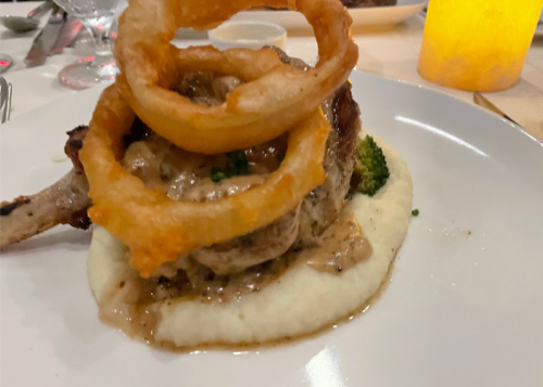 A plate featuring a pork chop topped with onion rings, served on creamy mashed potatoes with broccoli.