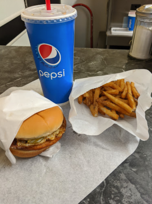 A burger wrapped in paper, a side of fries, and a Pepsi drink on a gray countertop.