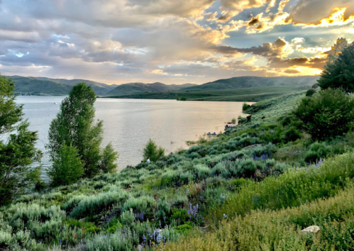 A serene lakeside view with lush greenery, mountains in the background, and a colorful sunset sky.