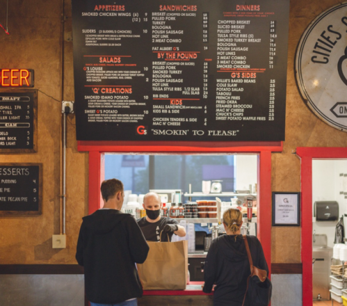A menu board at a restaurant with customers ordering takeout, featuring various food options and prices.