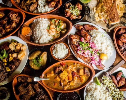 A vibrant spread of various dishes, including rice, seafood, meats, and garnishes, arranged on wooden tables.