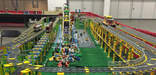 A colorful model train set with tracks, buildings, and a Ferris wheel, displayed in a large indoor space.
