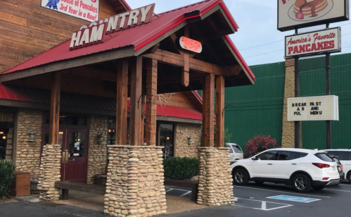 Exterior of a restaurant named "Ham N' Try," featuring a wooden entrance and stone pillars, with parked cars nearby.