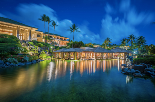 A serene resort at night, featuring thatched-roof pavilions by a calm waterway, surrounded by lush greenery and palm trees.