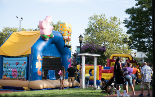 A colorful inflatable bounce house featuring cartoon characters, with people enjoying the park on a sunny day.