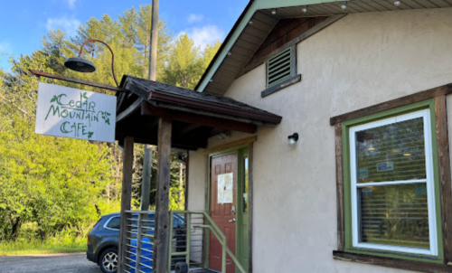 A cozy café building with a sign reading "Cedar Mountain Café" and a parked car outside. Green trees in the background.