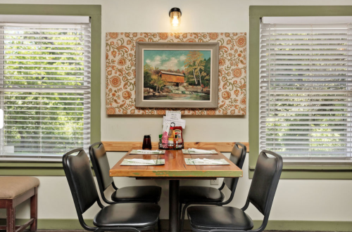 A cozy restaurant table set for four, with a painting on the wall and sunlight streaming through the windows.