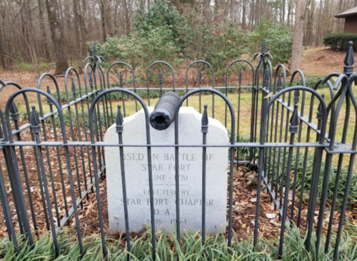 A gray gravestone surrounded by a black iron fence, marking a historical site from the Battle of Star Fort, 1863.