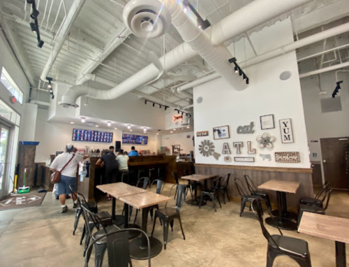 Interior of a casual dining restaurant with wooden tables, black chairs, and a counter where customers are ordering.