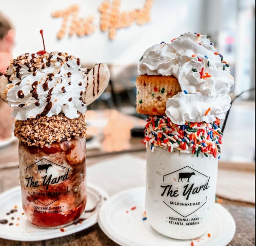 Two extravagant milkshakes topped with whipped cream, sprinkles, and a cherry, served in jars at The Yard Milkbar.