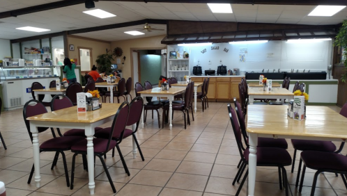 A spacious, empty dining area with wooden tables, purple chairs, and a serving counter in the background.
