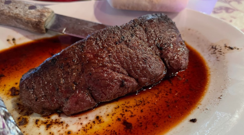 A perfectly cooked steak on a plate, glistening with sauce, accompanied by a knife.
