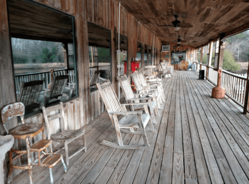 A rustic porch with wooden rocking chairs and a weathered wooden floor, surrounded by nature.