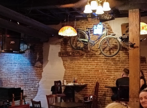 Cozy restaurant interior with brick walls, vintage bike decor, and warm lighting. Tables and chairs are set for dining.