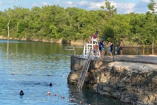 A group of people at a swimming area by a lake, with a lifeguard on duty and swimmers in the water.