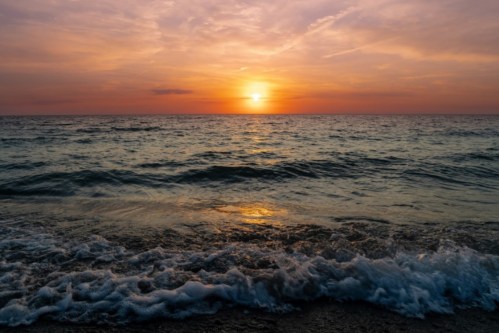 A serene sunset over the ocean, with gentle waves lapping at the shore and colorful clouds in the sky.