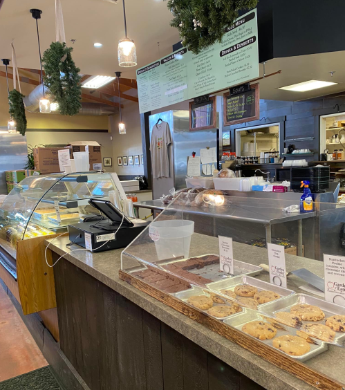 A cozy café interior featuring a display case of baked goods, a cash register, and a menu board above.