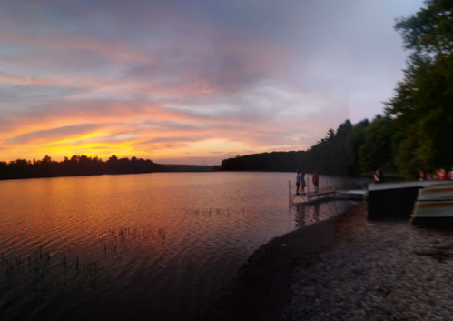 A serene lake at sunset, with vibrant colors in the sky and silhouettes of people on a dock.