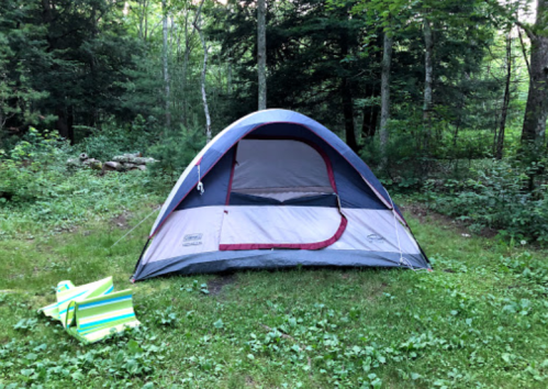 A tent set up in a lush green forest clearing, with two colorful folding chairs nearby.