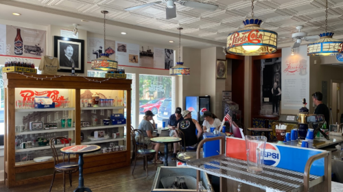 A vintage-style café with Pepsi decor, featuring patrons at tables and a counter, and nostalgic memorabilia on the walls.