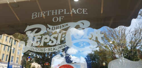 Sign on a window reading "Birthplace of Drink Pepsi-Cola" with decorative text and a price of 5 cents.