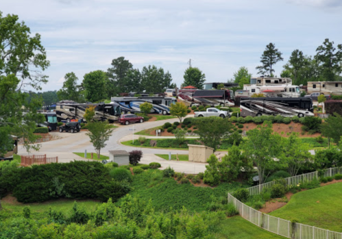 A scenic view of an RV park with multiple parked RVs surrounded by greenery and trees under a cloudy sky.