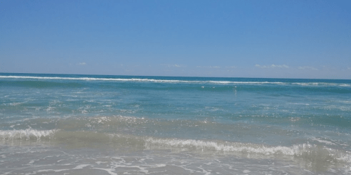 A serene beach scene with gentle waves lapping at the shore under a clear blue sky.