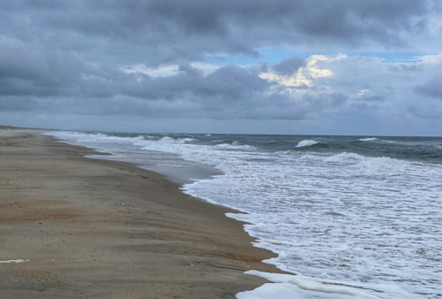 A sandy beach with gentle waves under a cloudy sky, creating a serene coastal atmosphere.