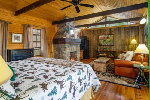 Cozy cabin interior featuring a wooden ceiling, stone fireplace, and rustic furniture with a warm, inviting atmosphere.