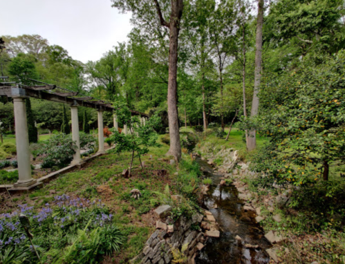A serene landscape featuring a stream, lush greenery, and stone columns amidst trees and flowers.