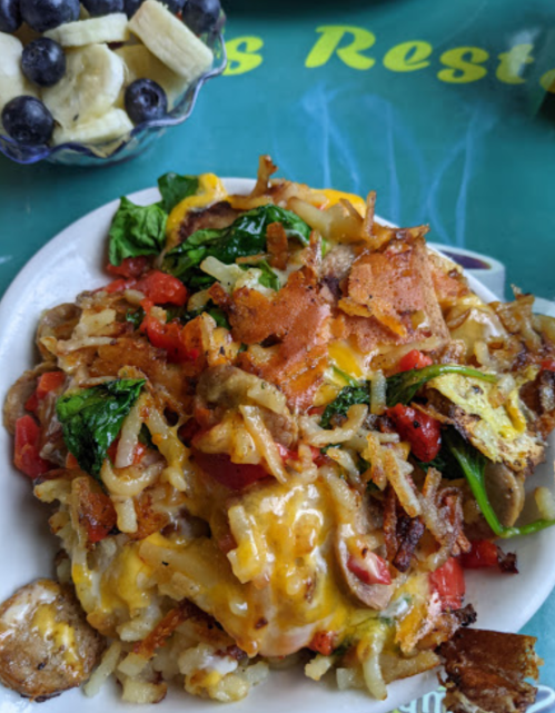 A hearty plate of loaded hash browns topped with cheese, bacon, vegetables, and herbs.