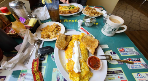 A table set with plates of omelets, toast, hash browns, coffee, and drinks in a cozy restaurant setting.