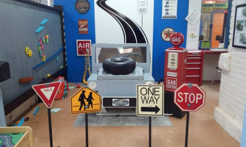A playful indoor scene featuring a toy jeep and various traffic signs, including stop and yield, in a colorful setting.