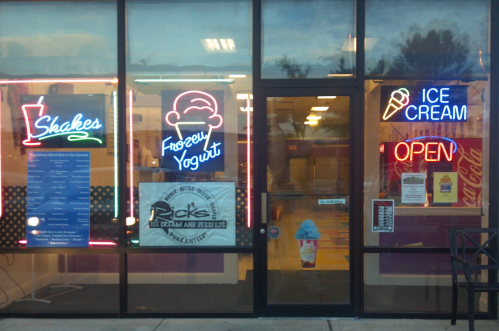 Brightly lit ice cream shop window featuring neon signs for shakes, frozen yogurt, and ice cream, with an "Open" sign.
