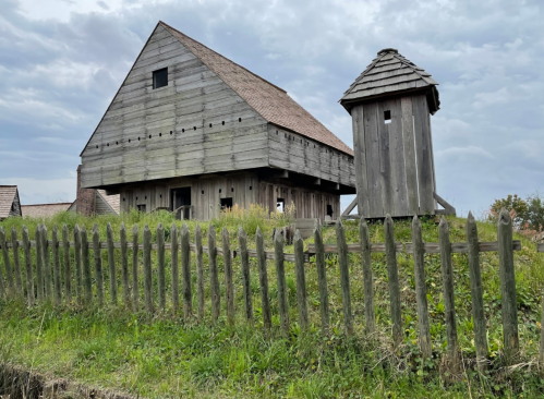 A wooden barn and a small tower surrounded by a wooden fence, set against a cloudy sky.