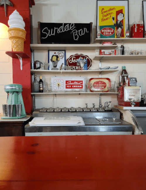 A vintage ice cream shop counter with a sundae bar sign, retro decor, and an ice cream machine.