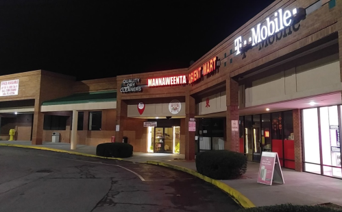A nighttime view of a shopping plaza featuring a T-Mobile store and a dry cleaners with illuminated signs.